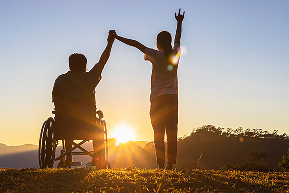 caregiver and man in wheelchair watch the sun set